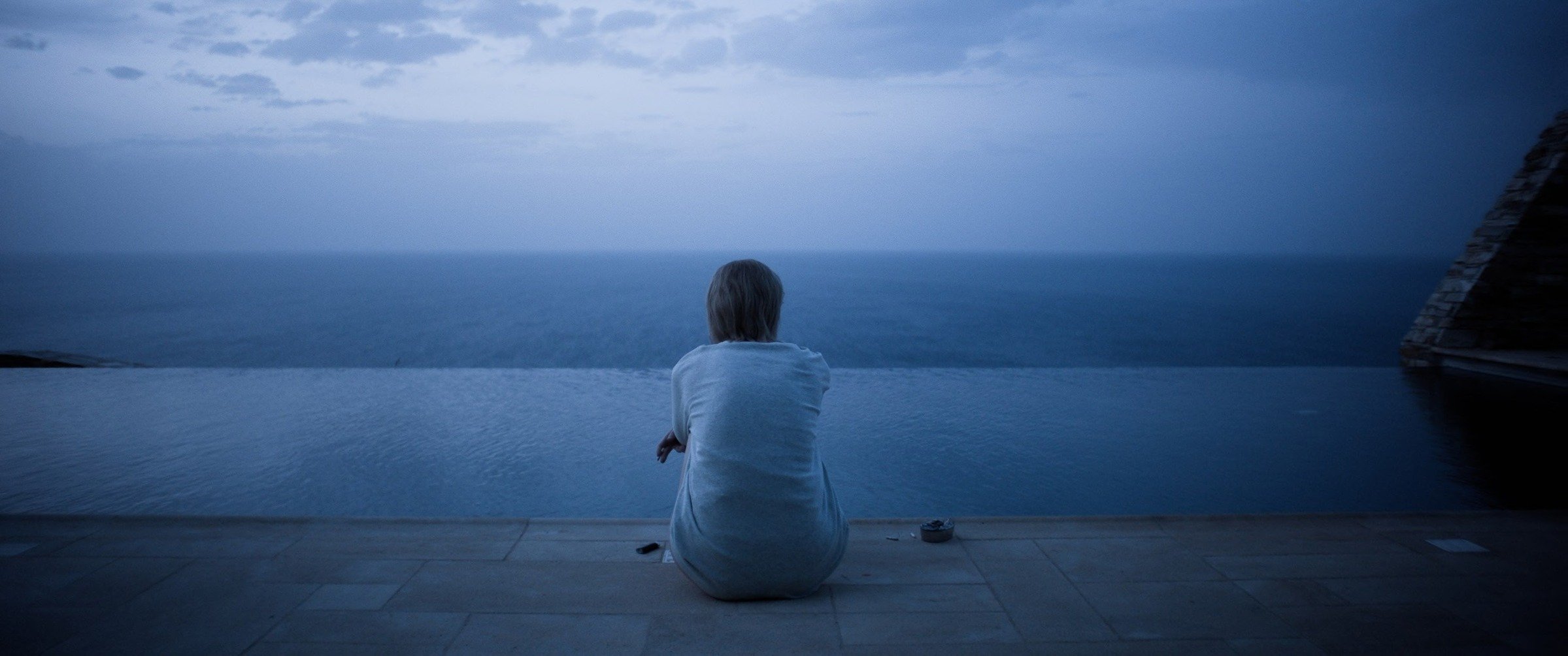 Dark blue, wide shot from the movie. Lola (Emma Laird) sits in the centre.
